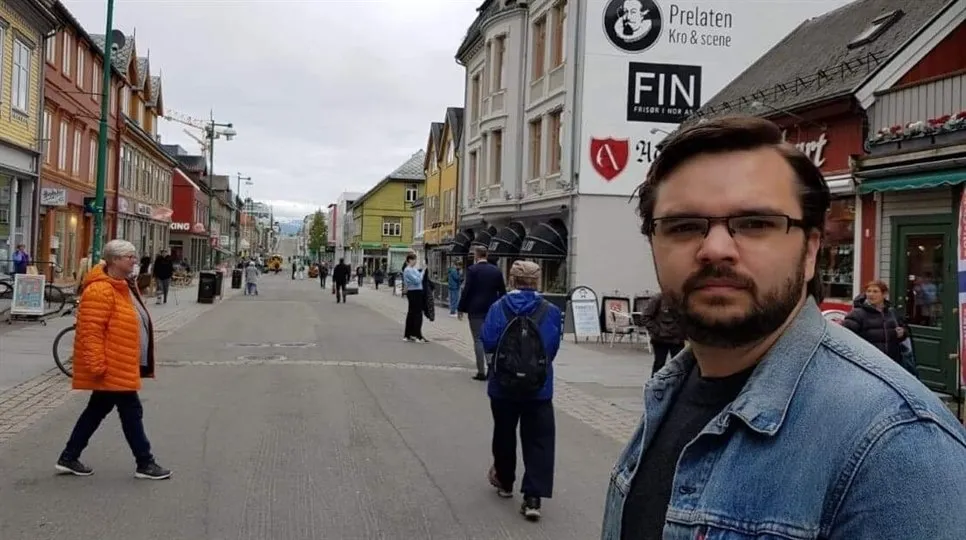 Joakim Pettersson står på en gata och tittar in i kameran. Andra människor och byggnader syns i bakgrunden.