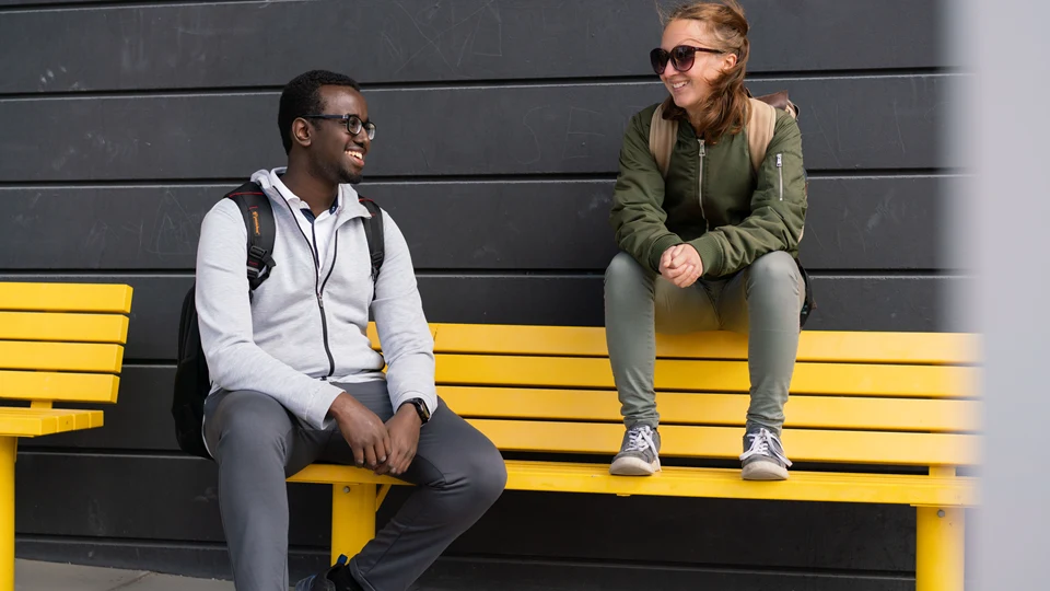 Två studenter som sitter på gul bänk. 