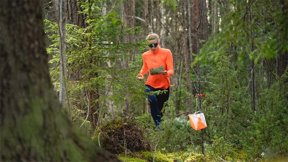 Orangeklädd kvinna utför orientering i skogen
