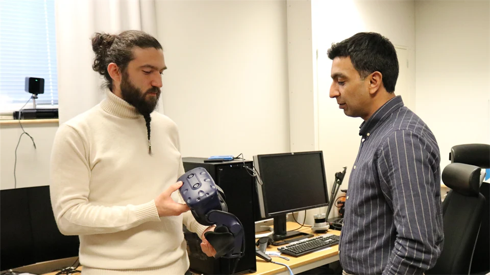Två män står tillsammans i en datasal. Den ena mannen håller i ett par VR-glasögon.