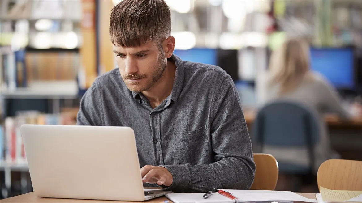Manlig student skriver på dator i studiemiljö