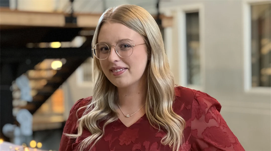 En ung kvinna med långt hår och glasögon tittar in i kameran.