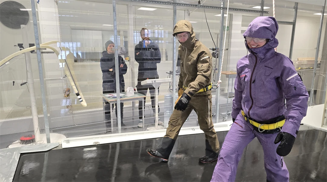 Två personer i färglada kläder går i en glastunnel medan två personer tittar på.