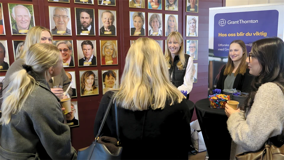 Studenter och företagsrepresentanter minglar framför en vägg prydd av många tavlor.