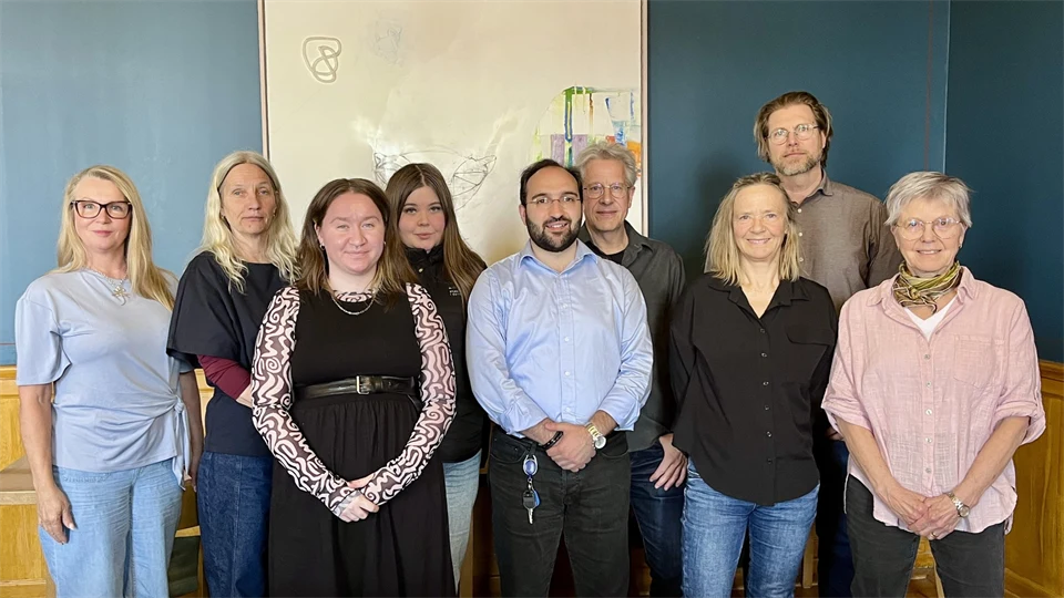 Nio personer står i en grupp och tittar in i kameran.