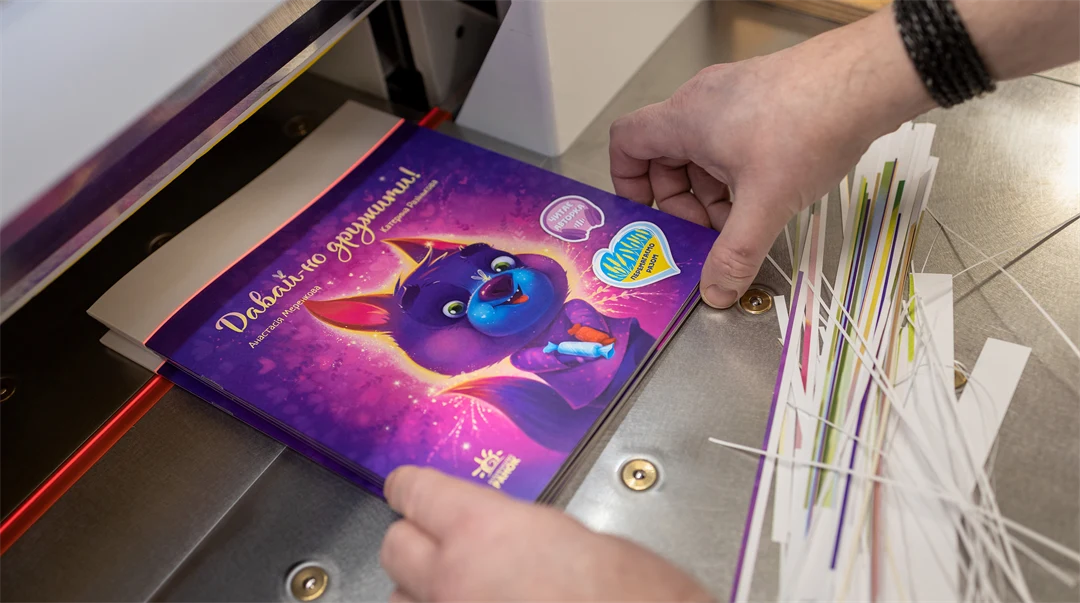 Två händer som håller i en barnbok vid en bokklipparmaskin