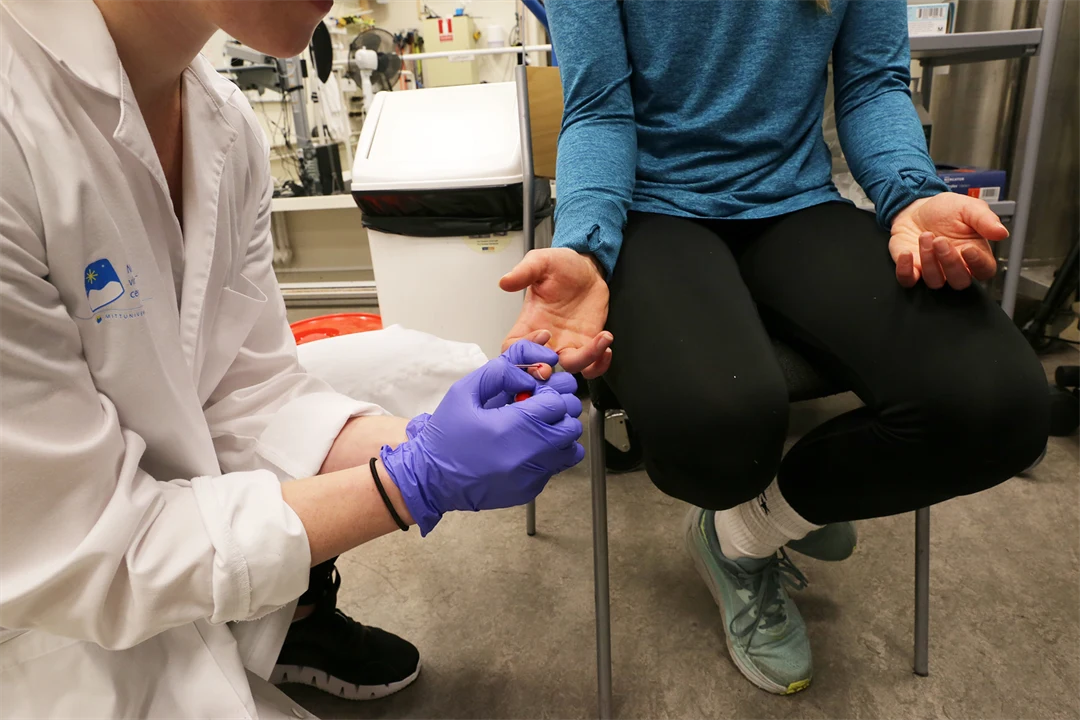 Person i labbrock tar blodprov på en person som sitter.