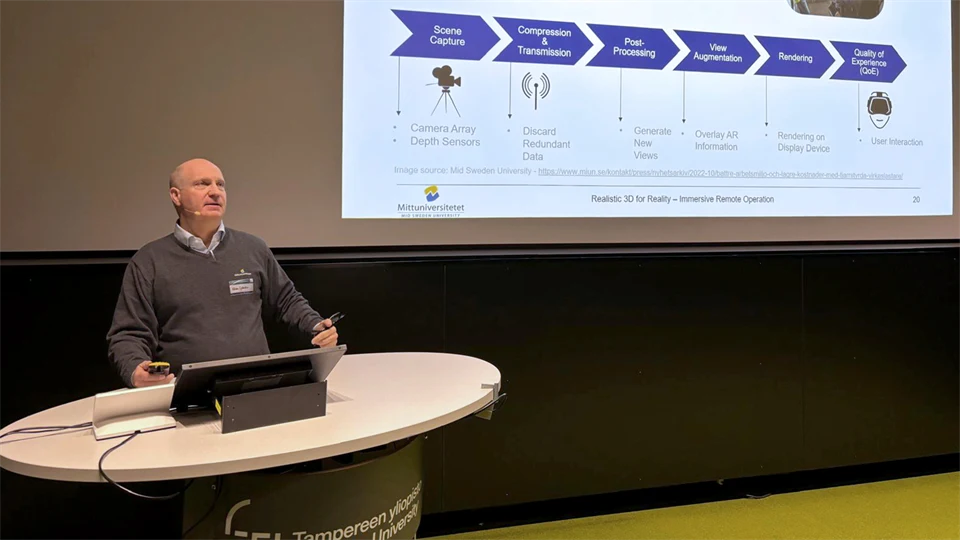 Man står vid ett podie och talar med en presentationsskärm bakom sig. 