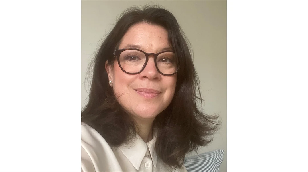 En kvinna med mörkbrunt hår och runda glasögon klädd i en vit sidenblus.