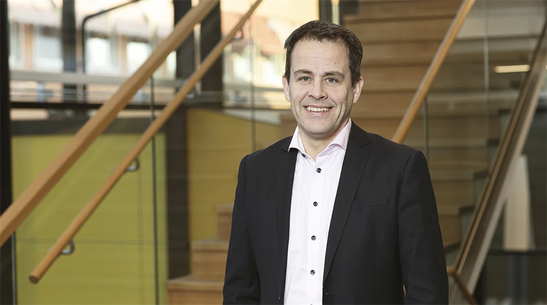 En mörkhårig man i svart kavaj poserar framför kameran.