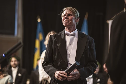 En finklädd man står med en professorsrulle i handen.