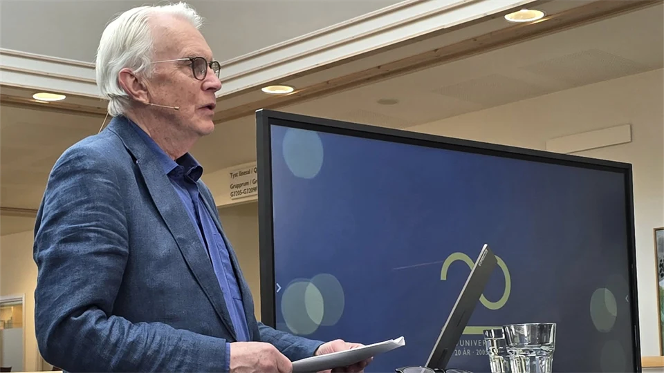 Gråhårig man i kavaj håller föredrag framför en bildskärm