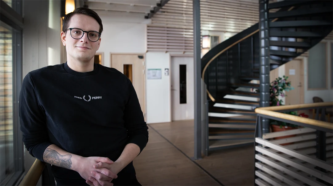 En man med svarta glasögon och svart tröja står vid ett trappräcke.