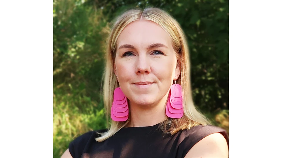 A woman with long blond hair, large pink earrings and wearing a black top.