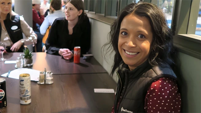 Ung kvinna med väst under mingel tillsammans med studenter i restaurang