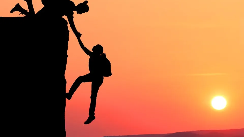 Ett par som klättrar, den ena hjälper den andra upp till en avsats. I bakgrunden solnedgång.