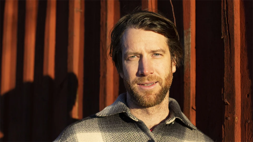 Portrait of a man outdoors with red panel wall in the background.