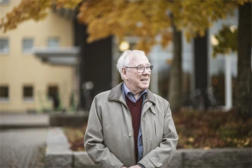 Herre i grå ytterrock står utomhus och ut mot omgivningen.
