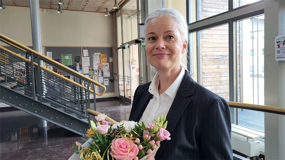 En ljushårig kvinna i svart kavaj med en blombukett i famnen.