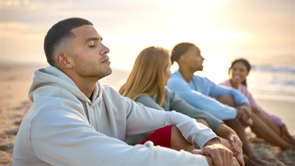 Två män och två kvinnor som sitter på en strand i solnedgång. 