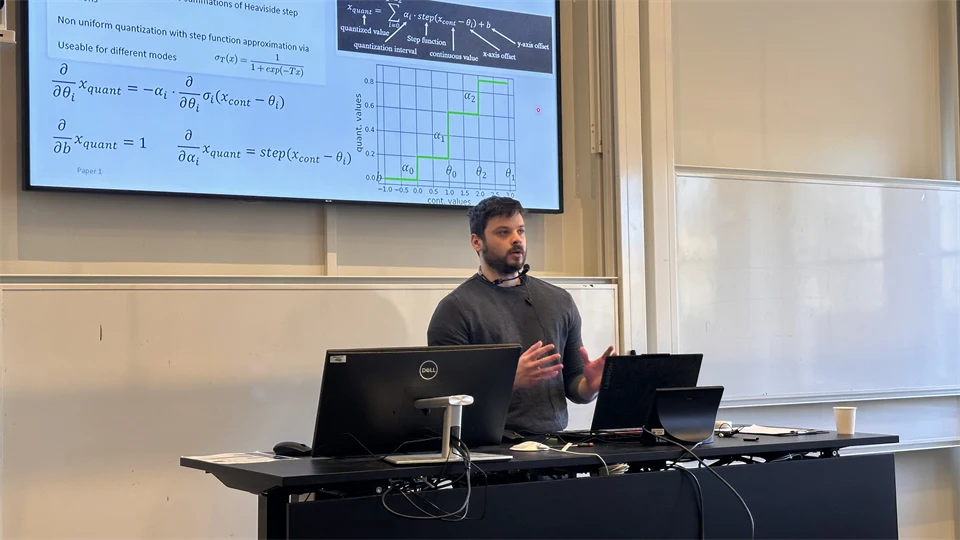 En man med mörkt hår står framför en skärm och pratar