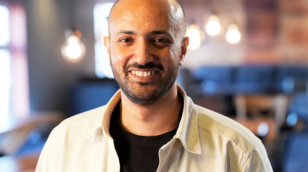 Porträtt av en man klädd i svart t-shirt och naturfärgad uppknäppt skjorta