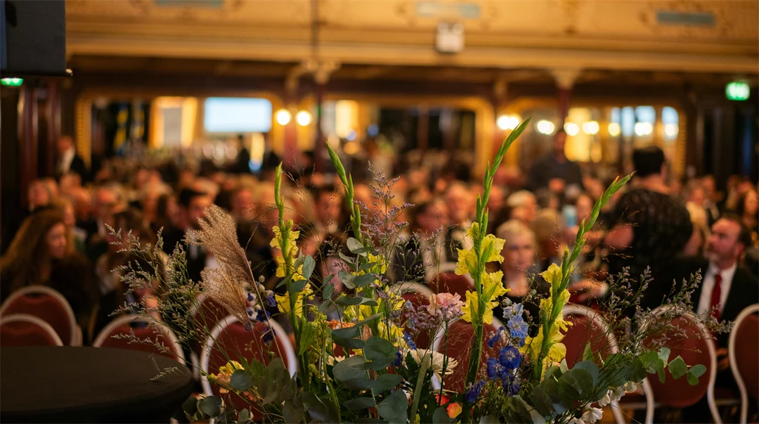 Blomsterarrangemang på en scen med uppradade stolar i bakgrunden.