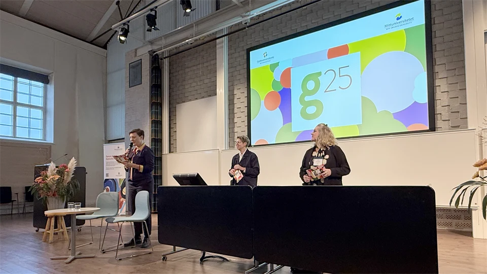 Tre kvinnor står på en scen, framför en stor skärm, och pratar inför publik.