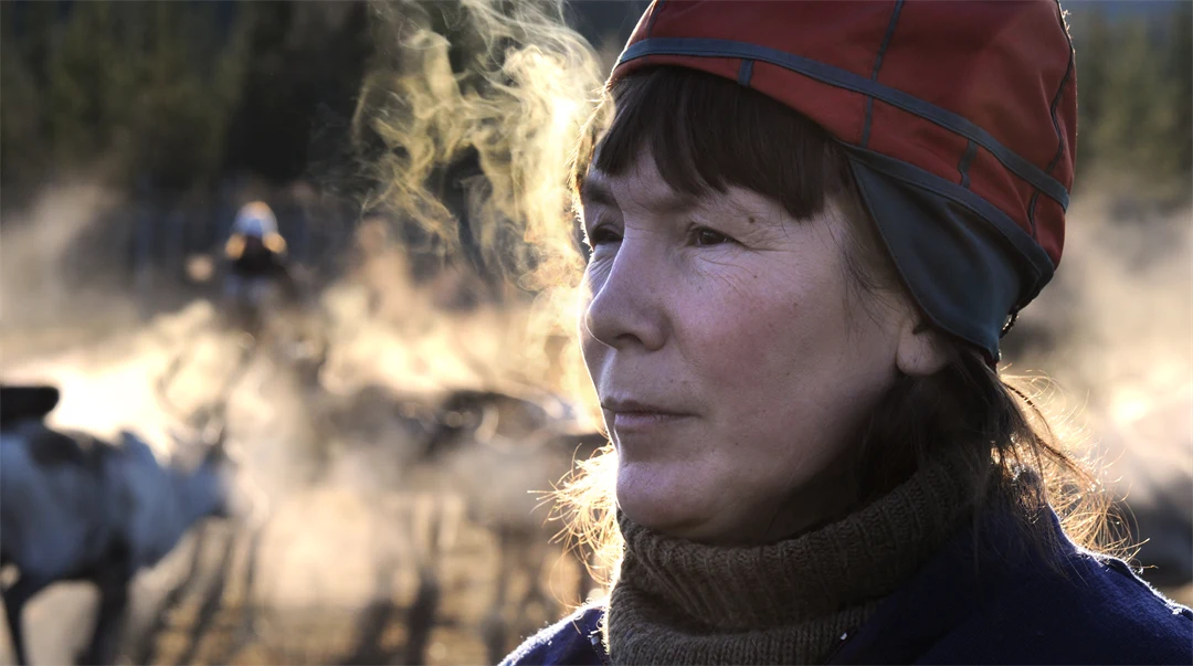 Kvinna i sydsamisk kvinnomössa andas så det bildas imma runt henne.