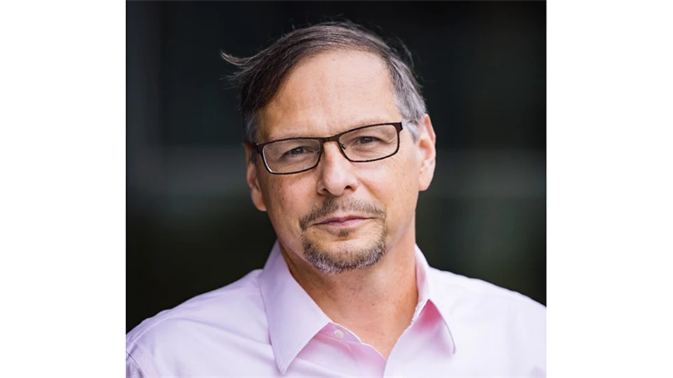 A dark-haired man in glasses, wearing a pink shirt.