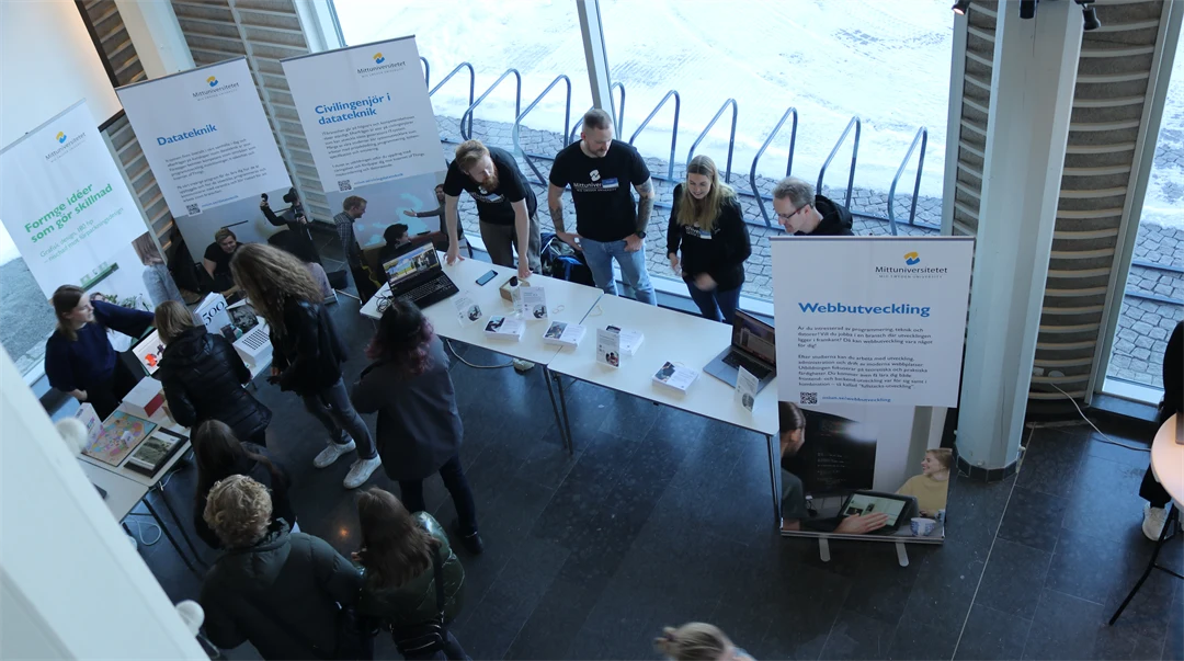 Studenter som står bakom ett bord och visar Mittuniversitetets utbildningar. 