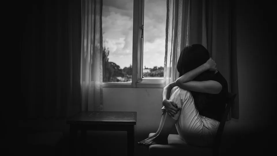 Depressed woman sitting on chair in a room near window.