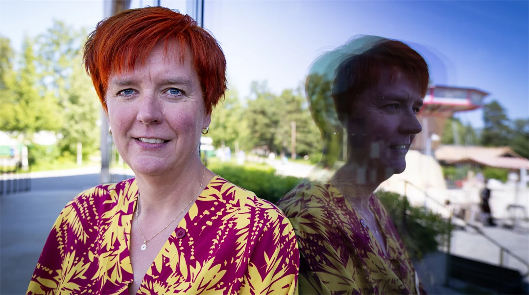 En kvinna sitter med ryggen mot ett fönster som återspeglar henne. 