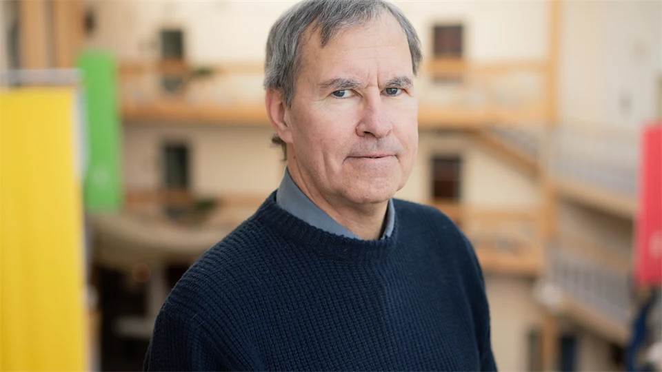 En man med grått hår, mörkblå tröja och mörkgrå skjorta. 