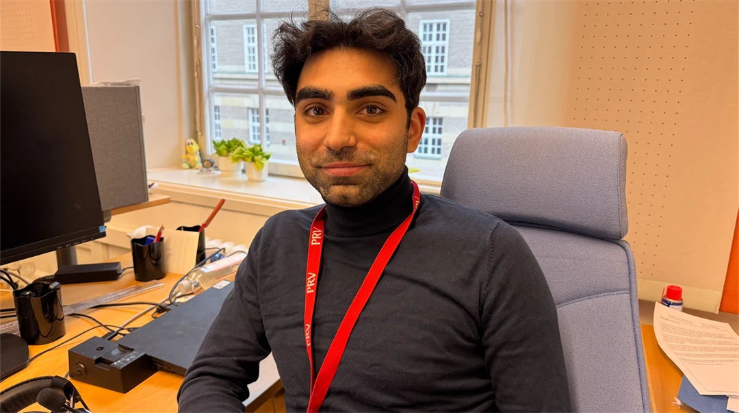 En man i mörk tröja sitter vid ett skrivbord.