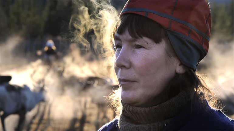 Kvinna i sydsamisk kvinnomössa andas så det bildas imma runt henne.