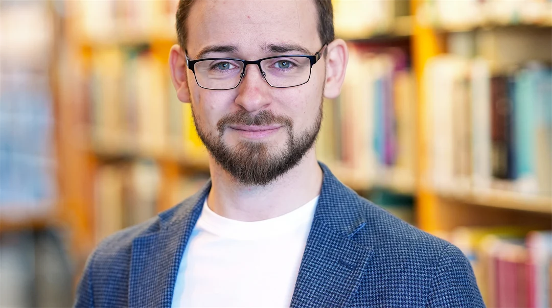 Porträtt av man, mörkt hår, blå ögon och skäggstubb. Klädd i blå kavaj och vit t-shirt 