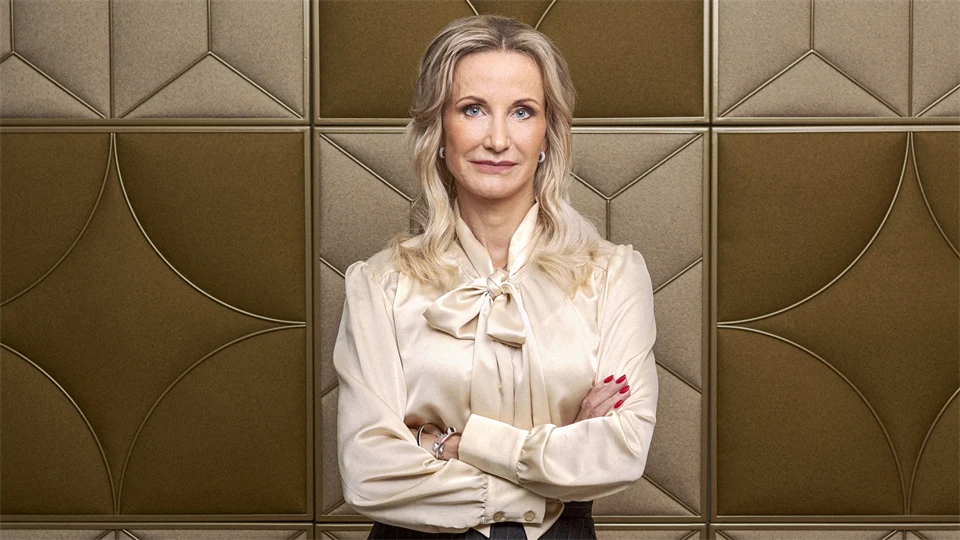 Porträttbild av kvinna med ljust hår och blus som står med armarna i kors.