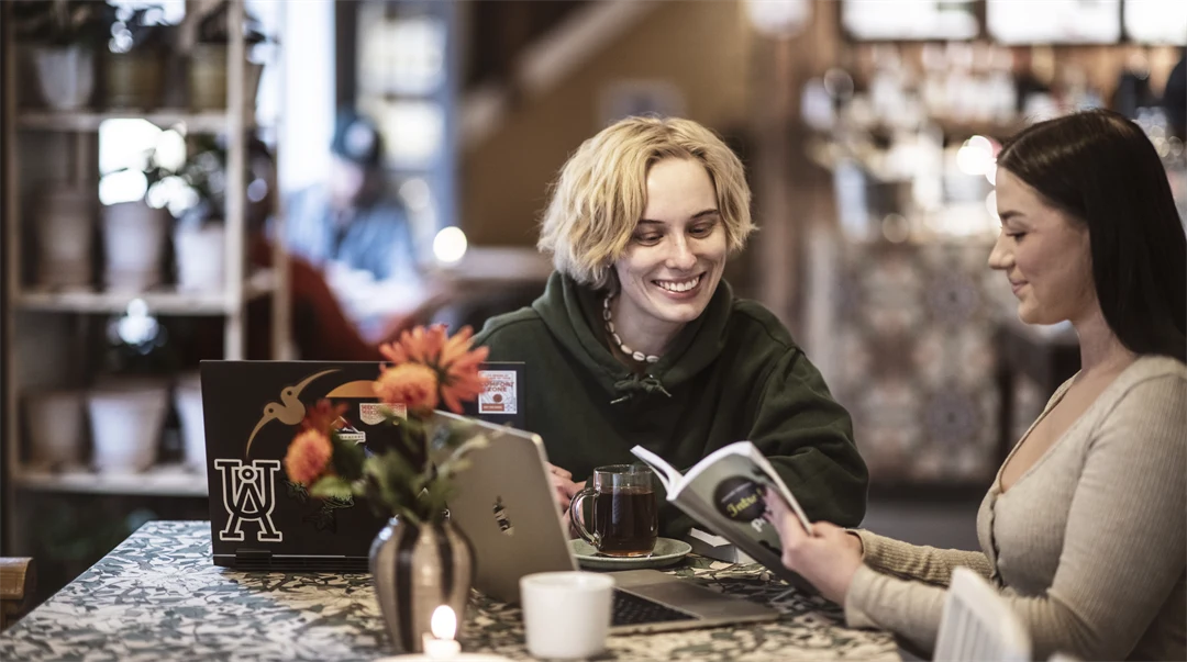 Två kvinnor sitter vid ett bord, tittar på en dator.