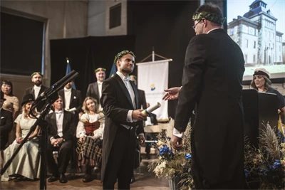 Två finklädda personer med lagerkransar står på en scen.