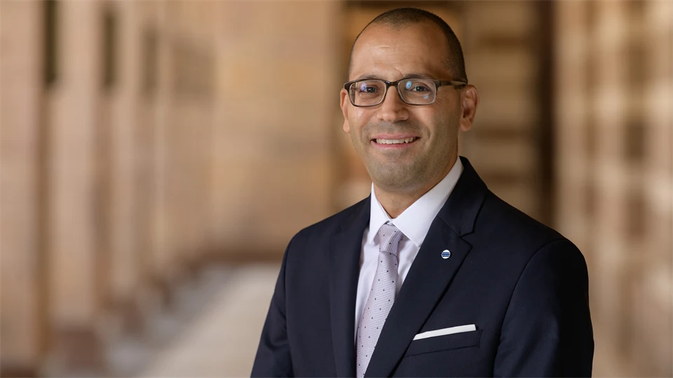 A well-dressed man with short hair and glasses smiles at the camera.
