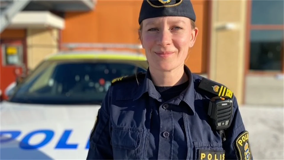 Kvinna i polisuniform står framför en polisbil