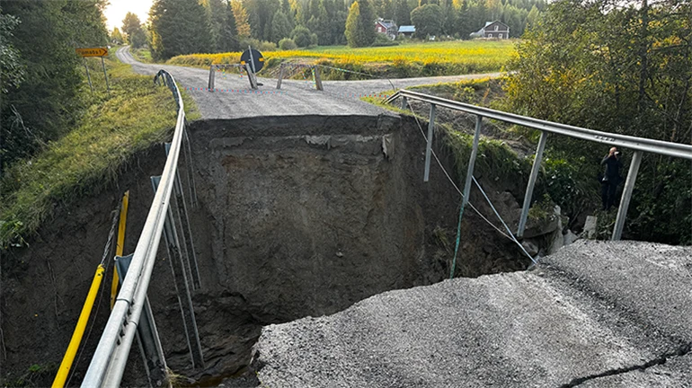 Collapsed road section with a large gap where the bridge fell, guardrails hanging over the edge.