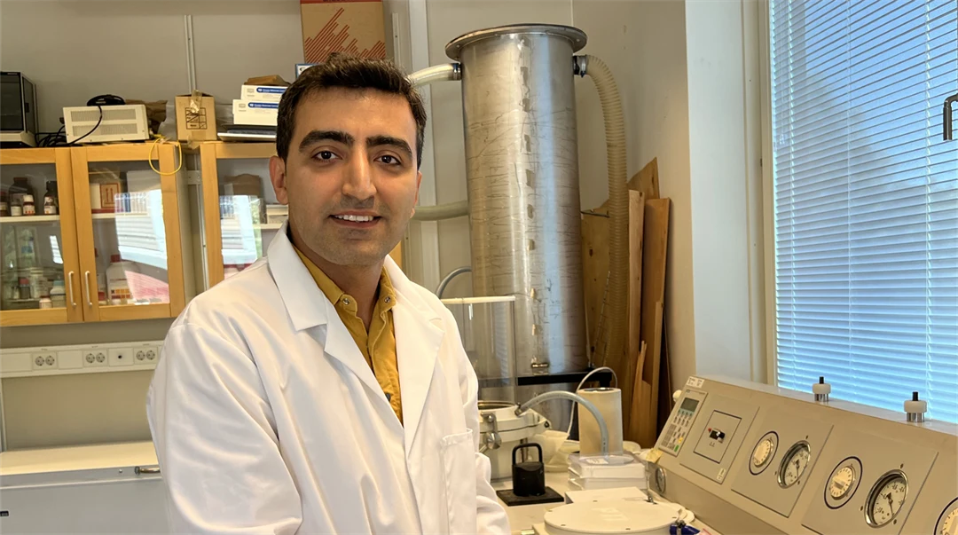  A man in a white coat in a research laboratory looks into the camera and smiles.