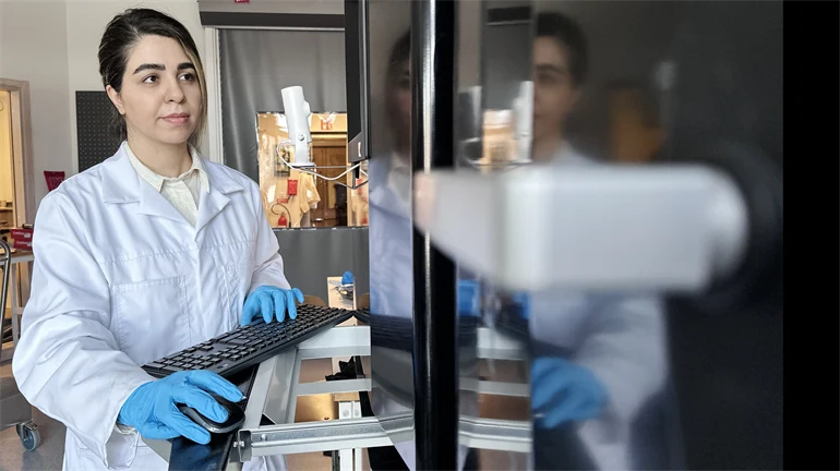 En kvinna i vit labbrock och blå handskar i labbet.