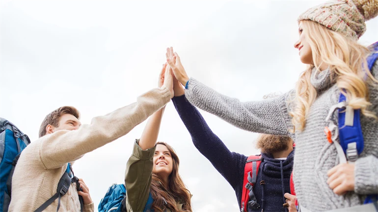 En grupp människor med ryggsäckar på sig står i en ring och gör en high five