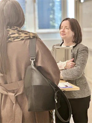 En kvinna i mörkt kort hår står i en föreläsningssal, studenter sitter på stolar vänd mot henne
