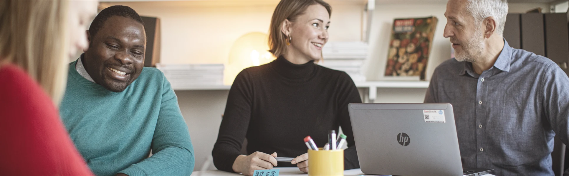 Fyra studenter runt ett bord som arbetar med en laptop och post-it lappar.