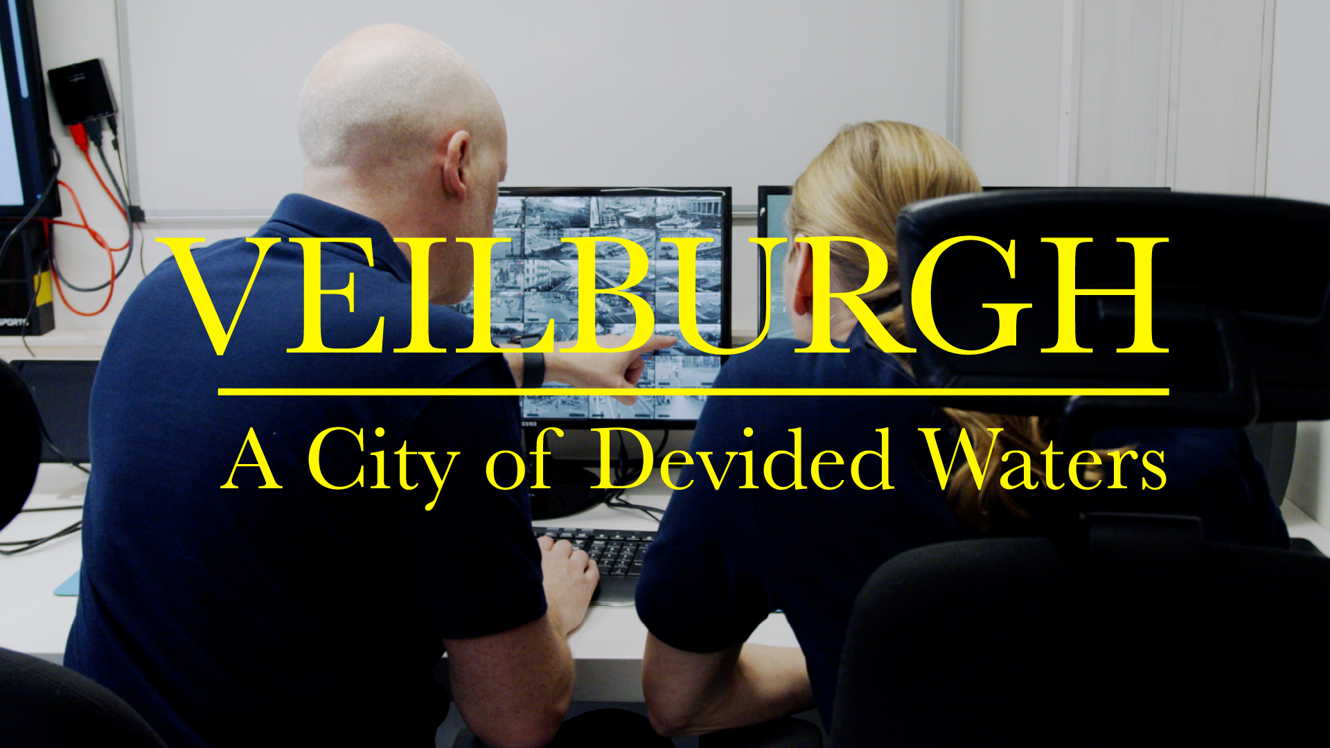 Two people are seated at a desk, looking at a computer screen displaying multiple surveillance images. Over the image, large yellow text reads: “VEILBURGH – A City of Devided Waters”.