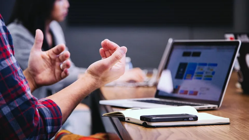 Gestikulerande händer i fokus, laptop och kvinna urfokus